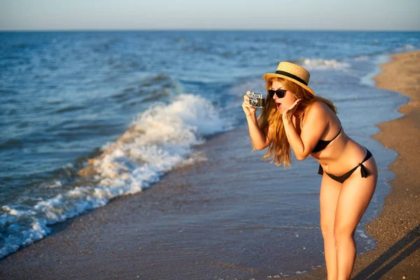 Klasik geçmişe dönük film kamerası olan genç bir kadın yaz tatilinde tropikal plajın tadını çıkarıyor. Bikini mayo giymiş kadın fotoğrafçı denizde eğlenirken fotoğraf çekiyor. Gerçekten yenilmez bir şekil kızı. — Stok fotoğraf