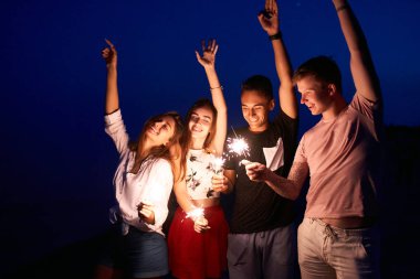 Arkadaşlar, yürüyüş bengal maytap ışıklar ellerinde ile deniz kenarında dans ve having fun gece boyunca parti. Havai fişek ile sahilde parti gençler. Ağır çekim steadycam vurdu.