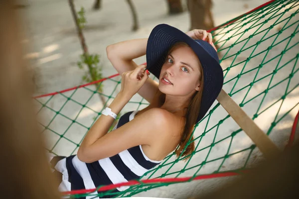 Frau entspannt sich in der Hängematte am tropischen Strand im Schatten, heißer, sonniger Tag. Mädchen blickt lächelnd in die Kamera — Stockfoto