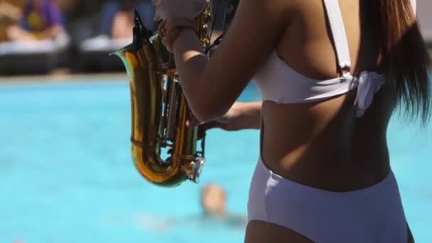 Attraente signora sassofonista sta giocando sul sassofono vicino piscina al beach club. Bella musicista sax girl in bikini bianco caldo balla e suona nel weekend party nella calda giornata estiva . — Video Stock