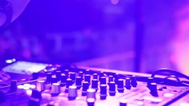 DJ, disko kulübünde müziği karıştırmak için ses konsolunu kontrol ediyor. Parmaklar düğmelere basar, güvertede elektronik müzik çalar. Gece kulübü dans partisinde renkli ışıklar gösteriliyor. Ağır çekimde kapat..