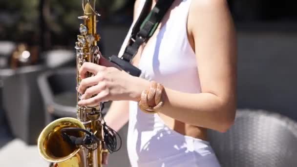 Aantrekkelijke saxofonist dame speelt op saxofoon in de buurt van zwembad bij beach club. Mooie sax meisje muzikant in hete witte bikini dansen en speelt op weekend feest op hete zomerdag. — Stockvideo