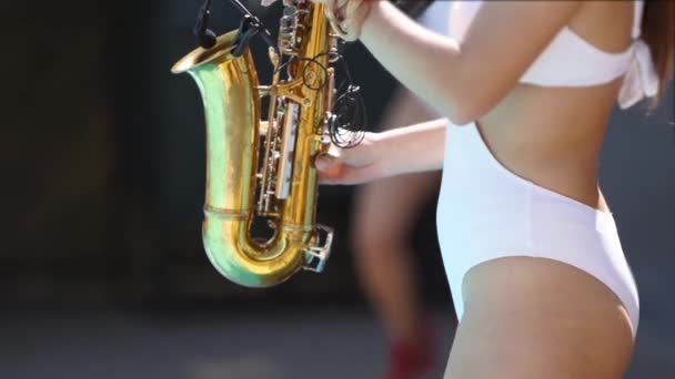 Aantrekkelijke saxofonist dame speelt op saxofoon in de buurt van zwembad bij beach club. Mooie sax meisje muzikant in hete witte bikini dansen en speelt op weekend feest op hete zomerdag. — Stockvideo