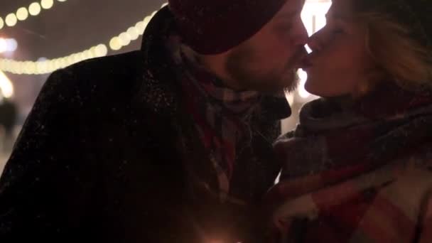 Para zakochanych bawi się z ogniem w rękach i całuje. Wigilia, Nowy Rok, Walentynki lub urodziny. Szczęśliwi ludzie imprezują w zimową noc ze śniegiem i girlandami na tle. — Wideo stockowe