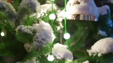 Karlı kış gecelerinde şehir meydanında parlak çelenkleri ve süslemeleri olan büyük bir Noel ağacı. Yakın plan. Dışarıdaki dekorasyonlarla dolu yeni yıl ağacının etrafında kameralar uçuşuyor. Işık Gösterisi