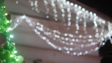 Karlı kış gecelerinde şehir meydanında parlak çelenkleri ve süslemeleri olan büyük bir Noel ağacı. Bokeh toplarıyla yakın çekim. Parlak dekore edilmiş yeni yıl ağacı. Sol Panorama.