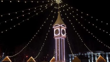 Noel ışıklarıyla süslenmiş saat kulesi, şehir meydanındaki yeni yıl pazarında ampul çelenkleri. Noel arifesinde dekoratif Big Ben 'in etrafında kameralar uçuşuyor. Zaman ve tatil kavramları.
