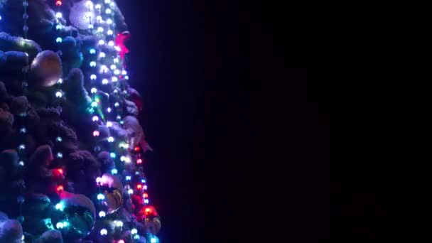 Gran árbol de Navidad con guirnaldas luminosas y decoraciones en la plaza de la ciudad en la noche nevada de invierno. Primer plano. Árbol de Año Nuevo decorado brillante lleno de decoraciones al aire libre. Un disparo estático. Copiar espacio . — Vídeos de Stock