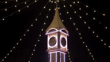 Noel ışıklarıyla süslenmiş saat kulesi, şehir meydanındaki yeni yıl pazarında ampul çelenkleri. Noel arifesinde dekoratif Big Ben 'in etrafında kameralar uçuşuyor. Zaman ve tatil kavramları.
