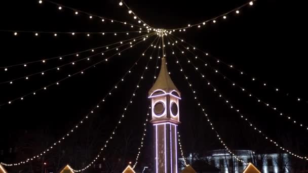 Torre del reloj decorada con luces de Navidad, guirnaldas bulbo en la plaza de la ciudad mercado de Año Nuevo. La cámara vuela alrededor del decorativo Big Ben en Nochebuena. Conceptos de tiempo y vacaciones . — Vídeos de Stock