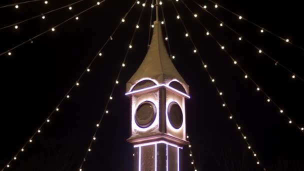 Torre del reloj decorada con luces de Navidad, guirnaldas bulbo en la plaza de la ciudad mercado de Año Nuevo. La cámara vuela alrededor del decorativo Big Ben en Nochebuena. Conceptos de tiempo y vacaciones . — Vídeo de stock