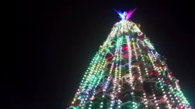 Karlı kış gecelerinde şehir meydanında parlak çelenkleri ve süslemeleri olan büyük bir Noel ağacı. Yakın plan. Açık havada süslemelerle dolu parlak bir yılbaşı ağacı. Panorama.