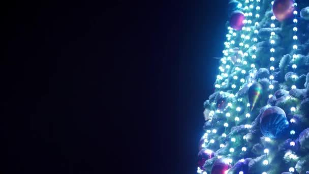 Gran árbol de Navidad con guirnaldas luminosas y decoraciones en la plaza de la ciudad en la noche nevada de invierno. Primer plano. Árbol de Año Nuevo decorado brillante lleno de decoraciones al aire libre. Un disparo estático. Copiar espacio . — Vídeos de Stock