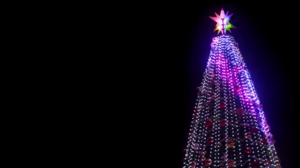 Nagy karácsonyfa fényes koszorúkkal és díszítésekkel a főtéren havas téli éjszakákon. Közelkép. Ragyogó díszes szilveszteri fa a szabadban. Statikus lövés. Fénymásolási hely. — Stock videók