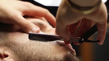 Profesyonel berber, müşteri sakalını ustura ile tıraş eder. Berber dükkanında eski moda bıçakla kesilmiş bir sakal. Yakışıklı maço adam stüdyoda sakalını kestiriyor. Yakın çekim..