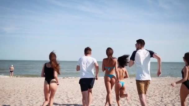 กลุ่มเพื่อนที่มีความสุขวิ่งไปที่น้ําทะเลและกระโดดบนชายหาดทราย คนร่าเริงมีความสนุกสนานบนชายหาดในวันที่แดดร้อน ชายหนุ่มและหญิงไปว่ายน้ําในมหาสมุทร 120 fps การเคลื่อนไหวช้า . — วีดีโอสต็อก