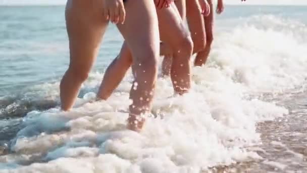 Slim piernas y pies femeninos caminando fuera de las olas de agua de mar en la playa de arena. Las mujeres bonitas se mueven frente al mar. Salpicaduras de agua y espuma en 120 fps en cámara lenta. Las niñas después de bañarse en el océano van a la orilla . — Vídeos de Stock