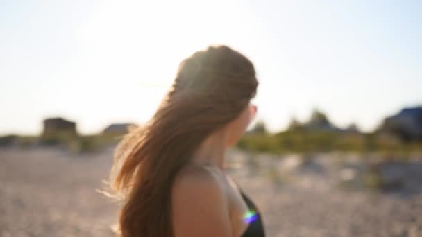Joven atractiva mujer rubia juguetona en traje de baño y gafas de sol caminando en una playa tropical soleada. Cabello largo bonita chica en bikini disfrutando de la caminata en la orilla del mar de arena en cámara lenta. Bengalas solares. — Vídeos de Stock
