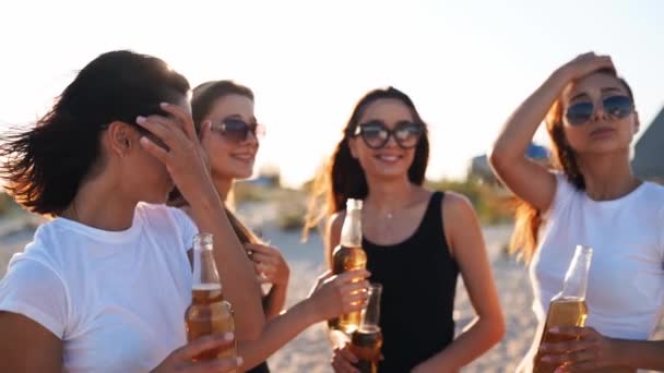 Hezké ženy v bikinách baví opékání nápojů a relaxaci na písečné pláži při západu slunce. Vhodné dívky v plavkách, sluneční brýle visící na mořském břehu s lahvemi od piva. Mladé ženy pijí limonádu. — Stock video