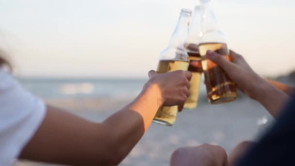 Groupe d'amis ont plaisir à griller, boire de la bière, se détendre sur la plage de la mer au coucher du soleil au ralenti. Jeunes hommes, les femmes aiment boire assis sur un sable lors d'une chaude soirée d'été. Les gens avec de la limonade. — Video