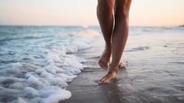İnce kadın bacakları ve ayakları kumlu sahilde deniz suyu dalgaları boyunca yürüyor. Güzel bir kadın deniz kıyısında sörf yapıyor. 120 fps yavaş çekimde su ve köpük sıçraması. Okyanusta yıkandıktan sonra kıyıya çıkan kızlar..