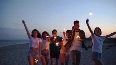 Arkadaşlar yürür, dans eder, ellerinde maytaplarla sahildeki partide eğlenirler. Genç gençler plajda havai fişekler ve bengal ışıklarıyla parti yapıyorlar. Yavaş çekim sabit kamera görüntüsü.