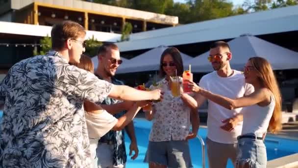 Group of friends having fun at poolside summer party clinking glasses with summer cocktails on sunny day near swimming pool. People toast drinking fresh juice at luxury tropical villa in slow motion. — Stock Video
