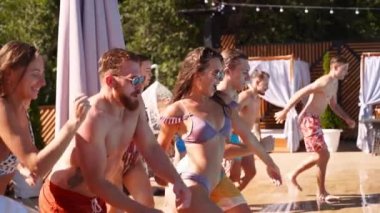 Lüks otellerde şişme şamandıralarla yüzme havuzunda zıplayan mutlu arkadaşlar. Mayolu gençler özel tatil köşkünde parti veriyorlar. Ateşli kızlar suya atlıyor. Yavaş çekim.