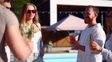 Bir grup arkadaş, havuz başında yaz partisinde bardakları tokuşturup güneşli bir günde havuz kenarında kokteyl içiyorlar. İnsanlar lüks tropikal villada yavaş çekimde taze meyve suyu içerek kadeh kaldırıyorlar..