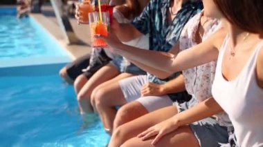 Şık güneş gözlüklü güzel bir kadın arkadaşlarıyla kadeh kaldırıyor havuz partisinde plastik pipet kokteyli içiyor. Bir grup arkadaş havuz kenarında oturup kadeh tokuşturarak eğleniyorlar. Yavaş çekim.
