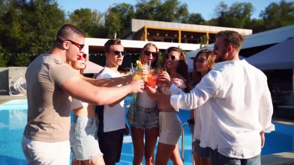 Grupp av vänner som har kul på poolside sommarfest klinkande glasögon med sommar cocktails på solig dag nära poolen. Folk skålar dricka färsk juice i lyxig tropisk villa i slow motion. — Stockvideo