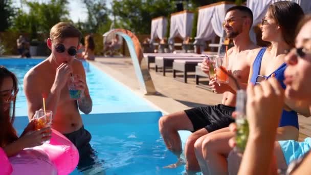 Eine multiethnische Gruppe von Freunden prostet zu, klimpert mit Gläsern und Cocktails auf einer Poolparty. Glückliche junge Leute in Badebekleidung tanzen, Clubbing mit aufblasbarem Flamingo, Matratzen im Luxus-Resort. — Stockvideo