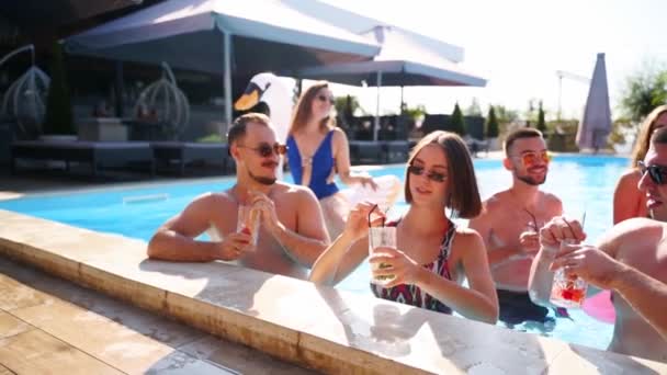 Vrienden die feesten met cocktails in het zwembad van de vakantievilla. Gelukkige jongeren in zwemkleding dansen, clubben met opblaasbare flamingo, zwaan, matras in luxe resort op zonnige dag. Langzame beweging — Stockvideo