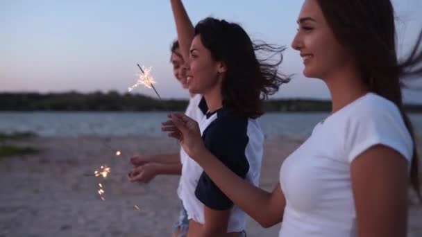 Kvinnliga vänner som går, dansar, har kul på kvällsfesten vid havet med tomtebloss i händerna. Unga tonårskvinnor festar på stranden med fyrverkerier, bengaliska ljus. Flickor i slow motion, steadycamskott. — Stockvideo