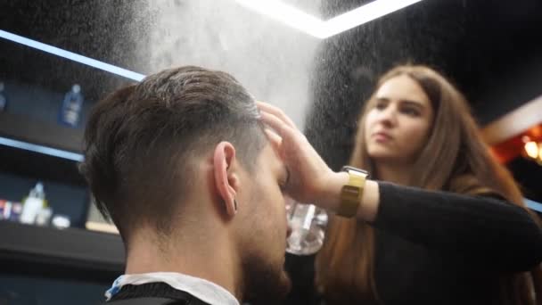 Barber pulvérise de l'eau sur les cheveux du client avant la coupe de cheveux et le coiffage dans le salon de coiffure. Coiffeur femme mouille les cheveux par pulvérisation et les peigne dans le salon de coiffure. Master utiliser pulvérisateur d'eau bouteille dans le studio de beauté masculine . — Video