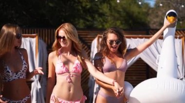 Bikinili seksi kızlar şişme kuğuyla yürüyorlar, yüzme havuzunda yüzüyorlar. Çekici, uyumlu, mayo giymiş kadınlar lüks bir tatil köyünde güneşli bir yaz partisinde rahatlarken eğleniyorlar. Slomo