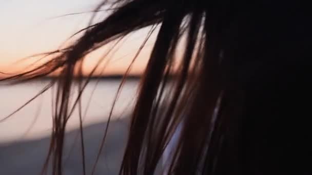 Chiudi indietro vista di marrone donna capelli tenero movimento in aria al tramonto estivo al rallentatore. Bruna o rossa donna in piedi su beachi al tramonto. Il vento soffia capelli ariosi che brillano all'alba. — Video Stock