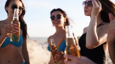 Bikinili güzel kadınlar gün batımında kumlu sahilde içki içerek ve dinlenerek eğleniyorlar. Mayolu kızlar, deniz kıyısında bira şişeleriyle asılı güneş gözlükleri. Genç dişiler limonata içer..
