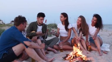 Arkadaşlar ateşin etrafında oturur, bira içer, gitar çalar, kumsalda sosis kızartırlar. Genç, melez bir grup kadın ve erkek birlikte şarkı söylüyor, sakallı bir adam alacakaranlıkta partide gitar çalıyor..