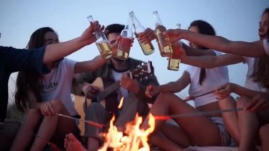 Arkadaşlar şenlik ateşinin etrafında oturur, bira şişelerini kızartır gitar çalar ve kumsalda sosis kızartırlar. Genç bir grup erkek ve kadın birlikte içki içiyorlar. Alacakaranlıkta gitar çalan adam..