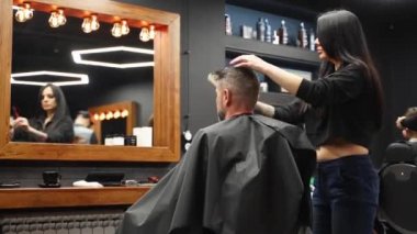 Çekici berber kız erkek saçını makas ve tarakla kesiyor. Müşteri hizmetinde çalışan kadın kuaför. Klasik berber koltuğunda oturan şık bir adam. Kuaför kadın moda saç kesimi yapıyor..