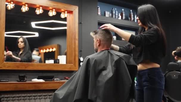 Menina barbeiro atraente cortando homens cabelo com tesoura e pente. Cortador de cabelo feminino trabalhando servindo cliente. Homem elegante sentado na cadeira de barbearia vintage. Mulher cabeleireira fazendo corte de cabelo na moda . — Vídeo de Stock