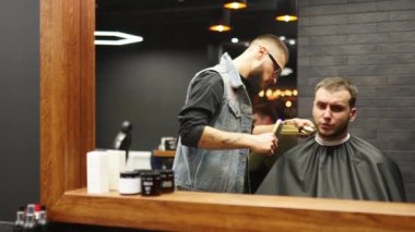 Gözlüklü berber berber dükkanında sakallı adamın saçını makasla kesiyor. Kuaförde hippi saç stili ve saç kesimi. Saçlarını budayarak. Kuaför kuaförde saç kesimi yapıyor. Ayna görüntüsü.