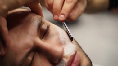 Profesyonel berber, müşteri sakalını ustura ile tıraş eder. Berber dükkanında eski moda bıçakla kesilmiş bir sakal. Yakışıklı maço adam stüdyoda sakalını kestiriyor. Yakın çekim..