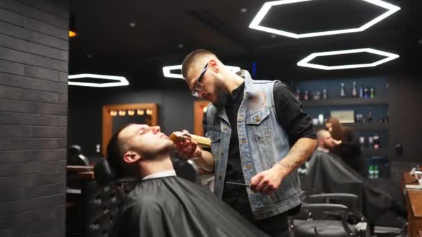 戴眼镜的理发师在理发店里用修剪工具修剪男人的胡子。理发店里的发型和理发。用剪子梳理头发.希斯特理发师在复古发廊理发. — 图库视频影像