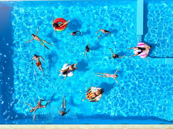 Aérien d'amis faisant la fête dans la piscine avec flamant rose gonflable, cygne, matelas. Les jeunes heureux se détendent dans un complexe de luxe par une journée ensoleillée. Vue d'en haut. Les filles en bikini bronzer dans un soleil. — Photo