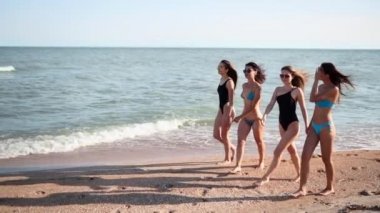 Bir grup güzel bayan arkadaş deniz kenarında, tropik kumsalda mayo giyerek yürüyorlar. Bikinili kadınlar yaz günü açık havada bronzlaşıp asılıyorlar. Mayolu kızlar yavaş çekimde gider..