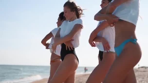 Egy csapat boldog női barát levetkőzik, belefutnak a tengervízbe, pólókat dobálnak a partra. Vidám lányok bikiniben szórakoznak a parton az óceán mellett. A fiatal nők úszni és fürdeni mennek. 120 fps lassított felvétel. — Stock videók