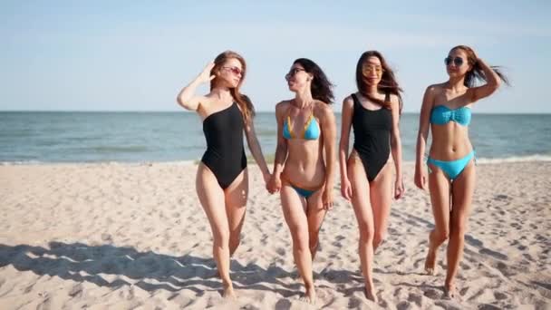 Groep van mooie vrouwelijke vrienden die plezier hebben wandelen over het zandstrand in zwemkleding. Interraciale vrouwen chatten en lachen op zomerse dag buiten. Meisjes in bikini en zwemkleding aan zee. — Stockvideo