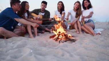 Arkadaşlar ateşin etrafında oturur, bira içer, gitar çalar, kumsalda sosis kızartırlar. Genç, melez bir grup kadın ve erkek birlikte şarkı söylüyor, sakallı bir adam alacakaranlıkta partide gitar çalıyor..